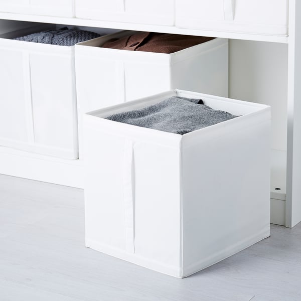 Three white SKUBB boxes in a wardrobe, storing items like blankets, socks, and sweaters. Each box has handles for easy access.