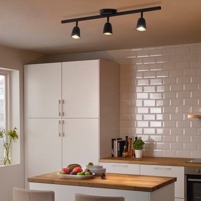 Modern kitchen with black ceiling lights, white cabinets, wooden counter.