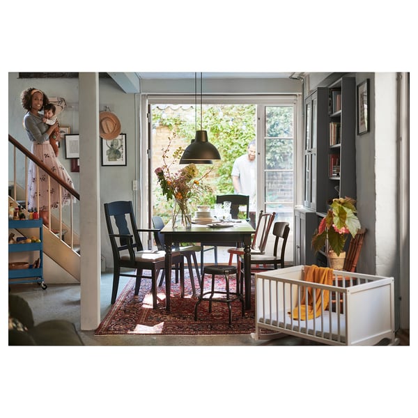 Family dining with wooden table, SKURUP lamp, person holding baby near stairs, person at door.