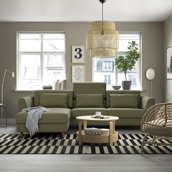 Modern living room with green sectional sofa, striped rug, coffee table, pendant lamp, and plant.