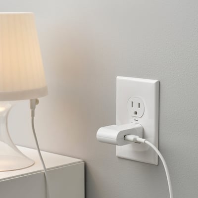 Plugged-in white lamp on the bedside, connected to a wall adapter offering usb charging.