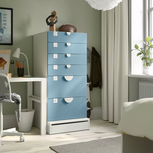 Blue SMÅSTAD chest with six drawers against green wall, next to white desk and window with curtains. Neatly organised with varied drawer sizes.