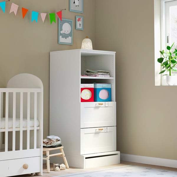 Small nursery with white SMÅSTAD bookcase and crib, colourful decorations, and a plant.
