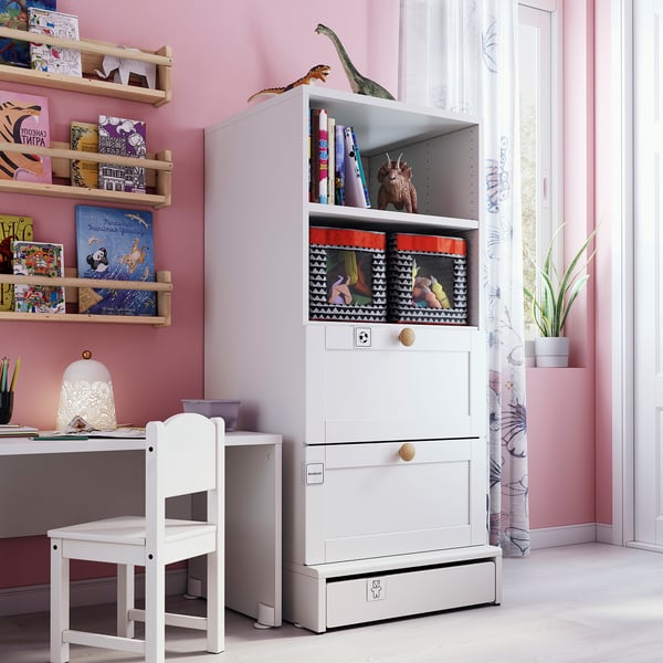 Small childs room with white SMÅSTAD bookcase, chair, desk. Pink walls, dinosaur toys, wood shelves with colourful books.