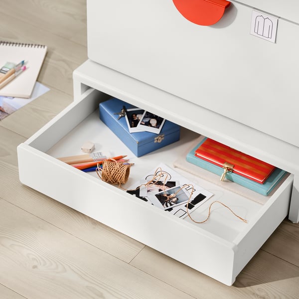 Open white drawer, showing blue box, red book, small basket, pins, and photos. Organised storage setup.