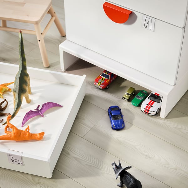 Kids room with white storage units and colourful toys. Dinosaurs and cars are placed around.