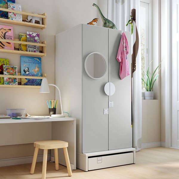 Kids room with white SMÅSTAD wardrobe, shelves filled with colourful books, small wooden stool, and desk with lamp.