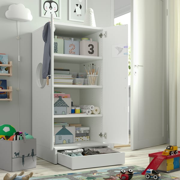 Small kids cabinet with open door revealing toys, books, art supplies. Soft-close hinges and adjustable feet for stability and safe reach.