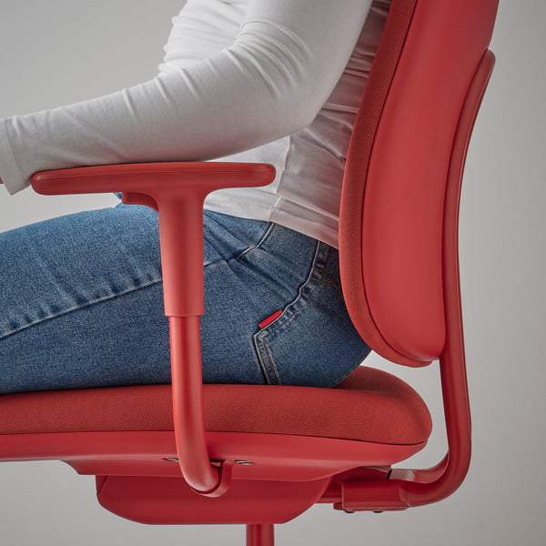 Red office chair with adjustable armrests, showing a persons legs and part of their torso sitting on it.