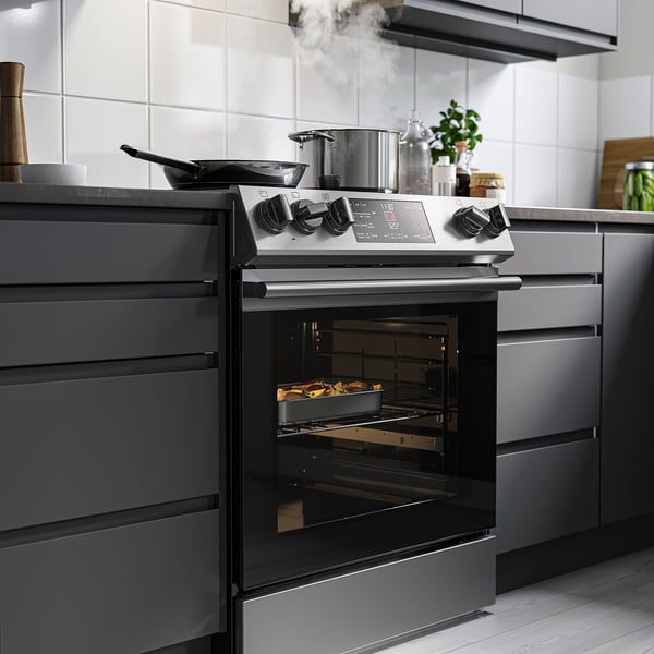 Modern kitchen with black range oven. Digital display, utensils on stovetop, dark cabinets.