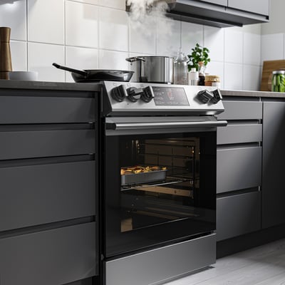 Modern kitchen with black range oven. Digital display, utensils on stovetop, dark cabinets.