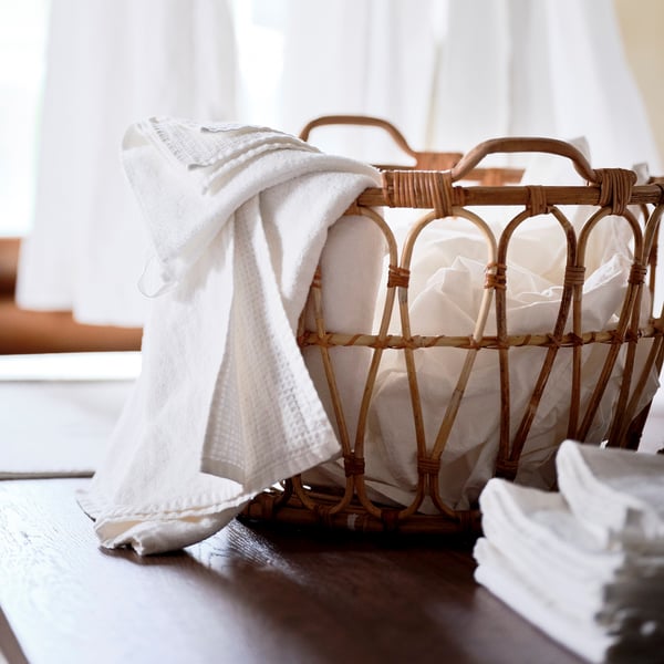 Woven bamboo basket holding white towels, perfect for storing blankets or cushions.
