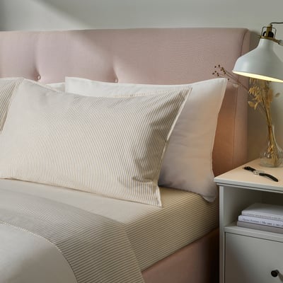 Bed with SOLFIBBLA striped beige sheets, pink pillows, white lamp, and books.