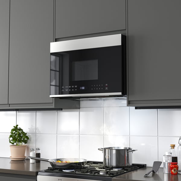 Modern kitchen with SOLNEBO stainless steel microwave oven installed above stove. White tiles, plant, and cooking utensils visible.