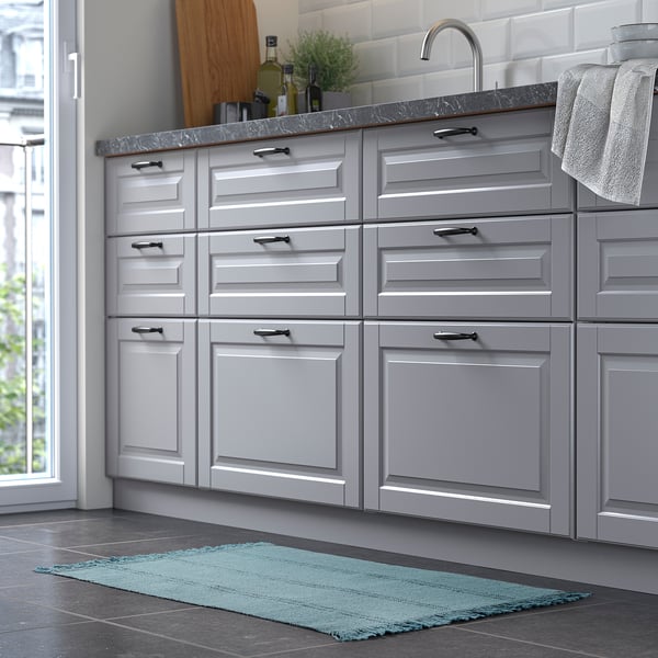 Kitchen with grey cabinets, sink and a blue rectangular rug on the floor.