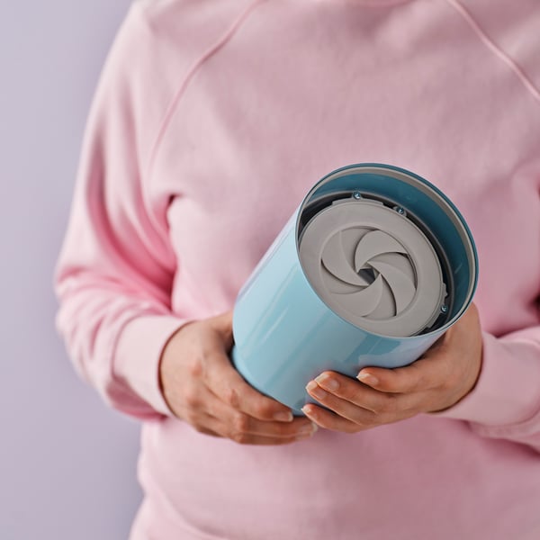 Hands holding a SPETSBOJ lamp, which has a spiral metal shade that adjusts light brightness.