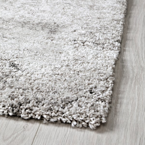 Fluffy grey rug corner on wooden floor, soft texture visible.