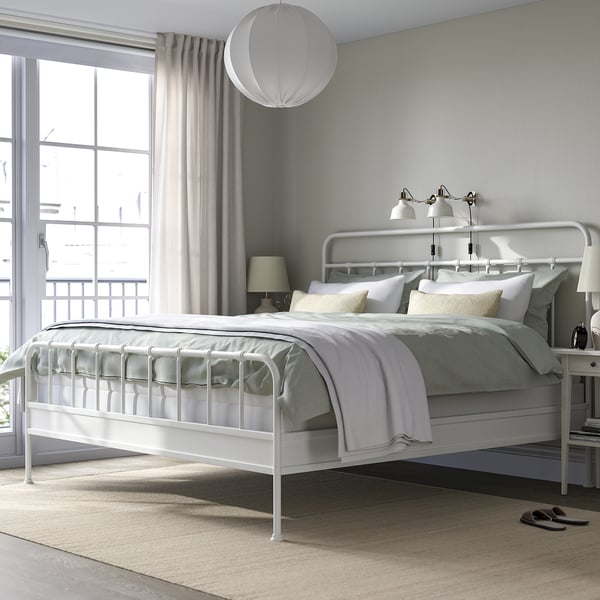 White STJÄRNÖ bed frame with curved headboard, steel details, minimalist decor, large window, and modern lamp.