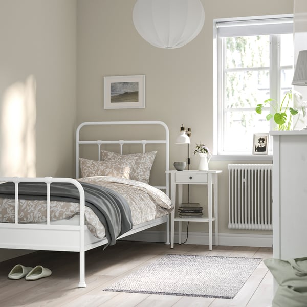 Cosy bedroom with STJÄRNÖ bed, patterned bedding, side table, lamp, plants, window, rug, slippers.