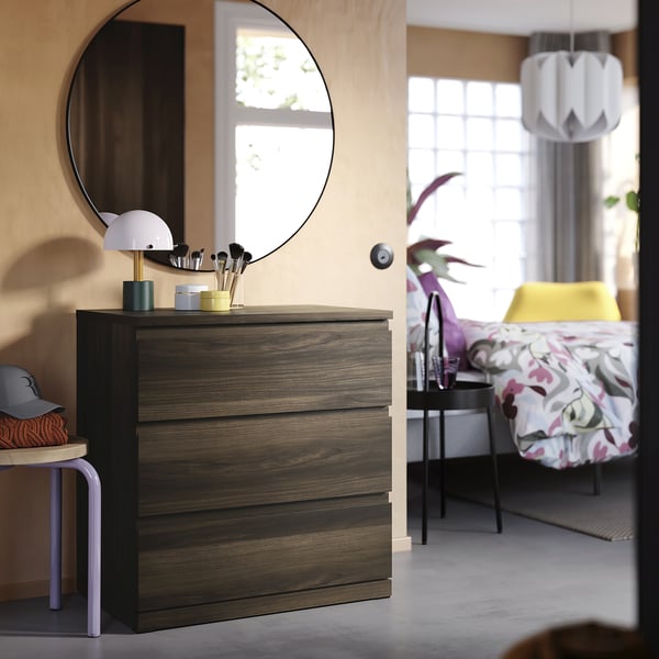 Bedroom scene with STORKLINTA dark wood dresser, mirror, colourful decor, and yellow bed.