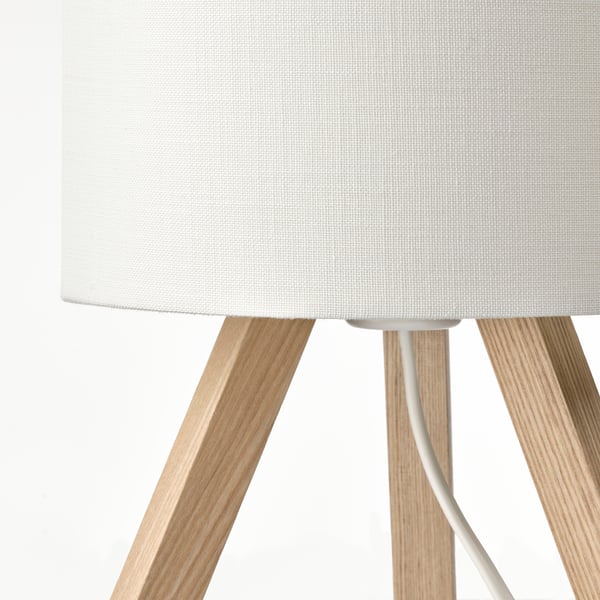 A stylish lamp with a white fabric shade supported by light wooden tripod legs.