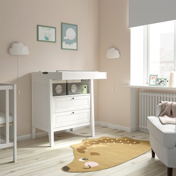 Baby nursery with SUNDVIK white chest, changing table, and deer rug. Two cloud lamps, art frames, and window with blinds. Light-colored wood floor.
