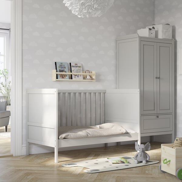 Modern grey and white nursery with SUNDVIK cot, cloud wallpaper, and grey storage cabinet. Light grey rug, bookshelf, and plush toys around.