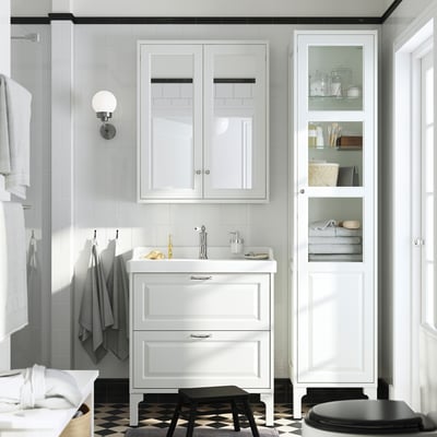 White TÄNNFORSEN glass-door bathroom cabinet with bevelled panels, wall-mounted for floor space savings, offers vertical storage and dust protection.