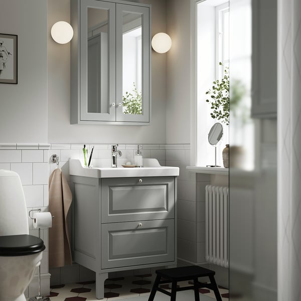 Modern grey bathroom vanity with drawers, sink, toilet, wall mirror, and black stool.