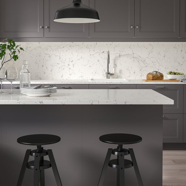 Modern kitchen with marble-patterned glass wall and worktop, dark grey cabinets, and black stools under a narrow island.