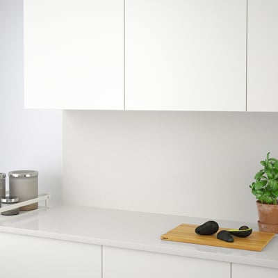 Modern kitchen counter with avocados on a wooden cutting board, a potted plant, and a glass-encased candle holder.