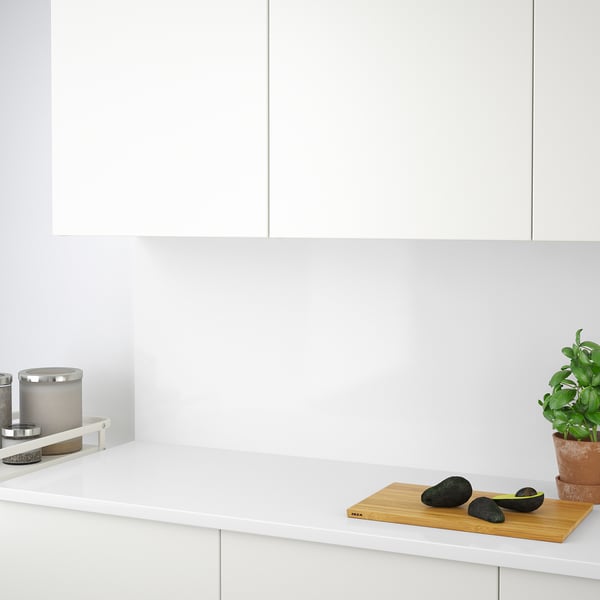 Minimalist kitchen counter with avocados on a cutting board, potted plant, and candle in a holder, showcasing clean and organised workspace.