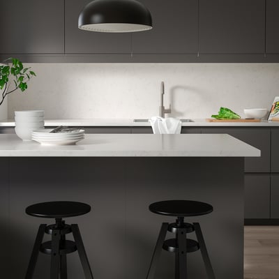 Modern minimalist kitchen with white marble counter, black bar stools, and sleek dark cabinets.