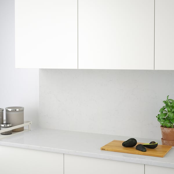 Modern kitchen with white cabinets, TÄRNHULT wall panel, avocados on bamboo board, candle, and plant.