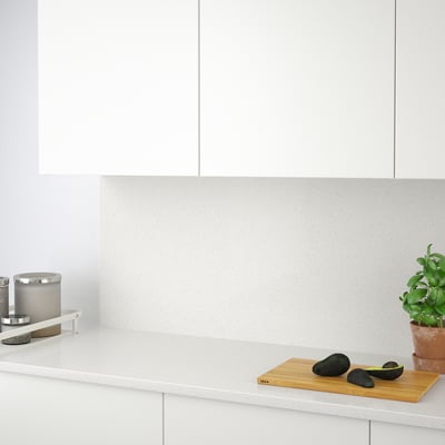 Minimalist kitchen with white cabinets. Countertop cut avocados, herbs, and stainless containers. Glass backsplash protects walls.