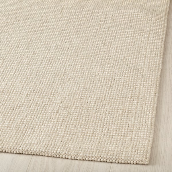 Beige textured jute rug displayed on wooden floor. Flat-woven, natural fibres visible.