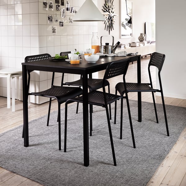 Modern kitchen with black dining set, food, white backsplash, grey rug.