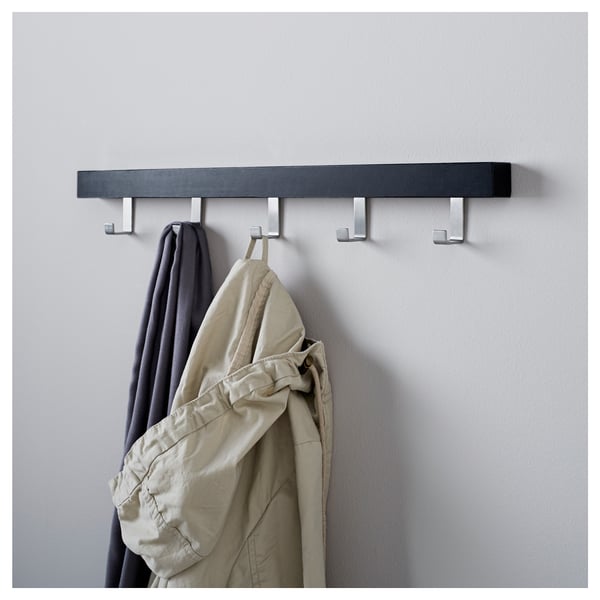 A wall-mounted coat rack, TJUSIG series, holds a grey jacket and beige coat on its metal hooks. The dark wooden shelf organises clothing efficiently.