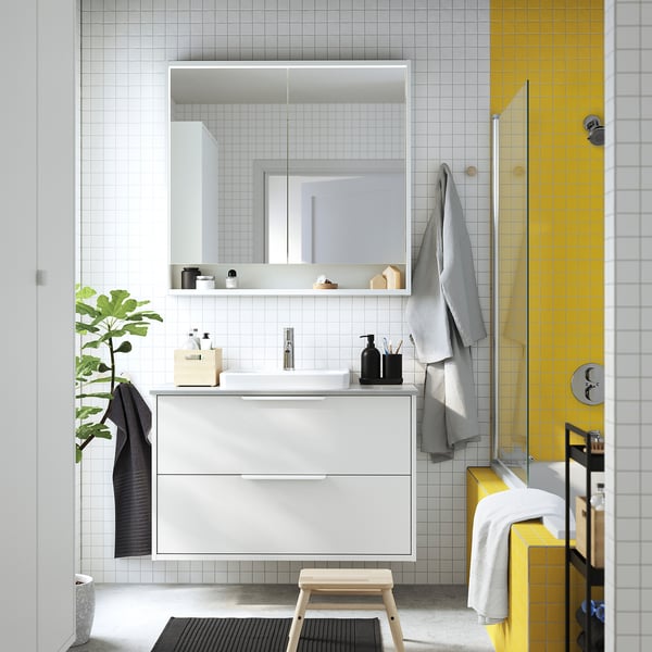 Modern bathroom with yellow, white tiles. White TOLKEN cabinet, mirror, built-in sink. Towels, plant. Bright, organised.