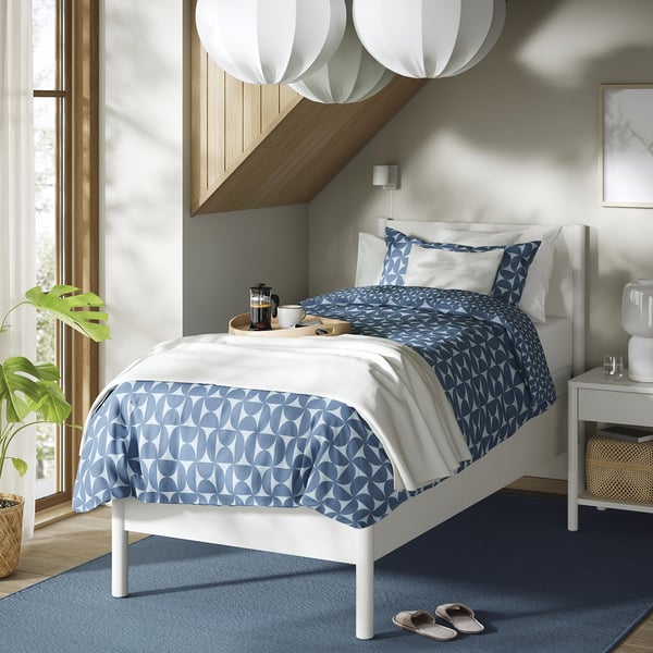 TONSTAD off-white bed with blue pattern, cosy rug, warm room, plants, light wood.