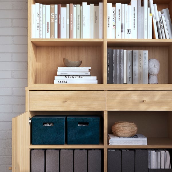 Wooden bookcase with shelves and drawers. Teal boxes, brick wall.