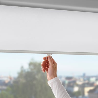 Image shows a hand adjusting a cordless roller blind. It blocks light and offers soft-closing feature.