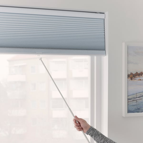 A hand adjusting a TRIPPEVALS block-out blind, preventing light from entering through a window.