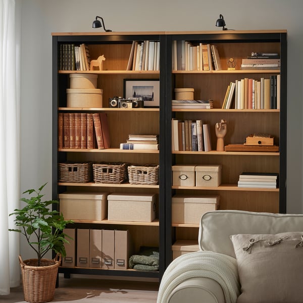 Wooden bookshelves with lamps, books, boxes, decor, armchair, plant.