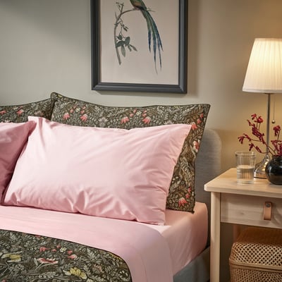 Bed with pink ULLVIDE percale sheets, floral pillows, framed art, lamp and bedside table. Sheets are cotton/lyocell blend, soft, breathable.