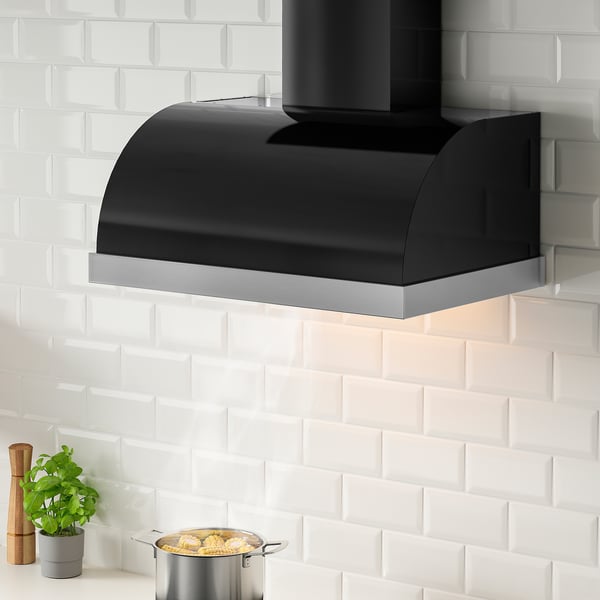 Black UNGDOMLIG kitchen hood mounted above a stove, contrasts against white brick backsplash, smaller than the surrounding tiles.