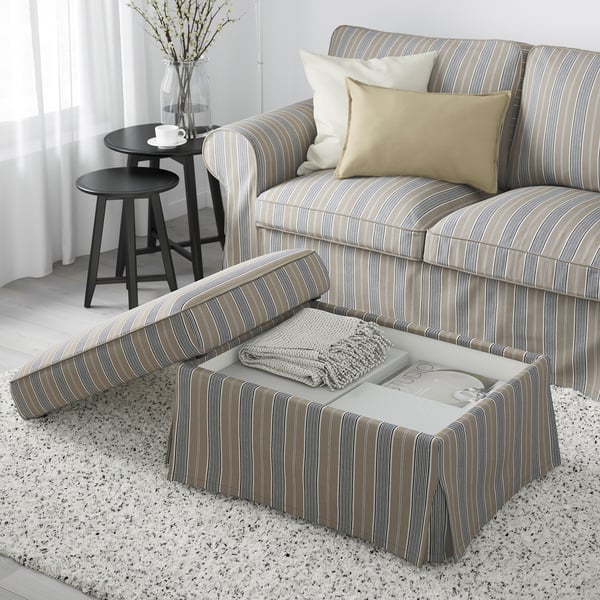 Striped upholstered ottoman with storage, featuring pillows and a cosy blanket on top.