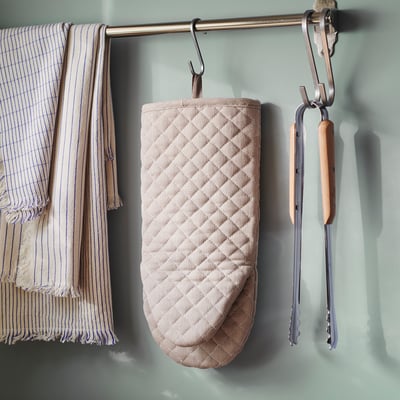 Beige oven mitt hangs on hook with kitchen tools.