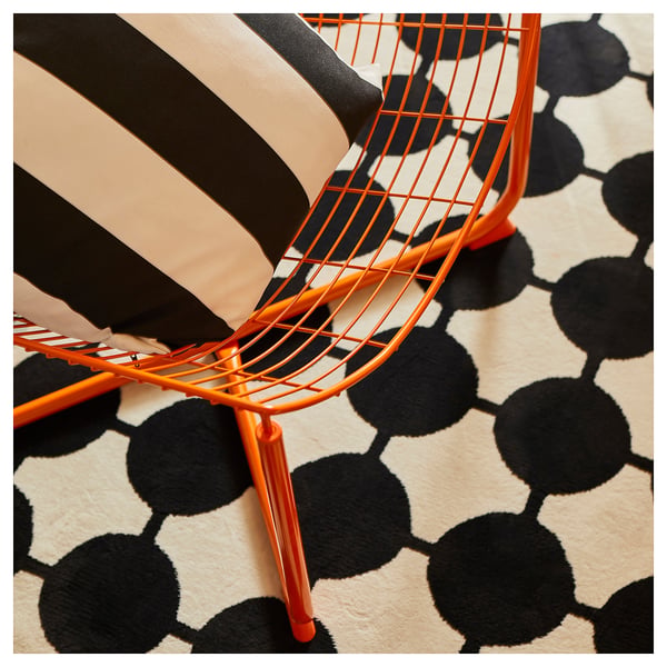 Bright orange wire chair on black and white dotted rug, modern design.