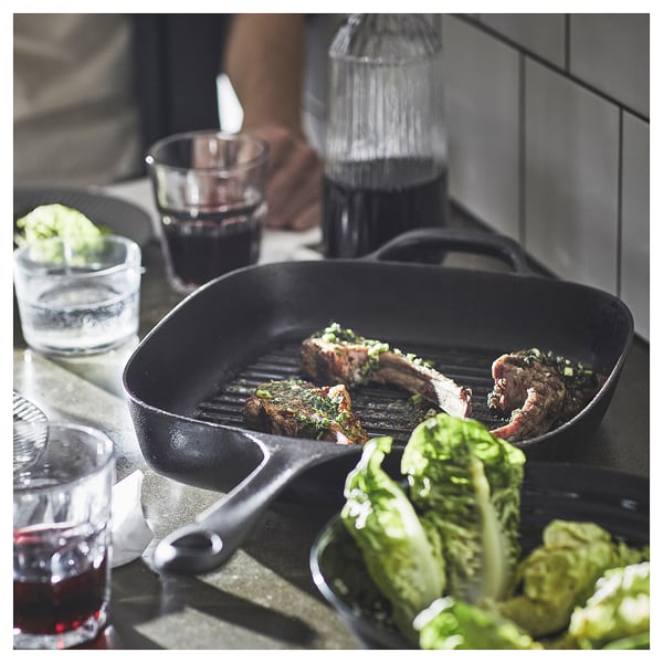 Black cast iron grill pan with steak, glasses of red wine, and lettuce. Cooking scene with dish preparation.